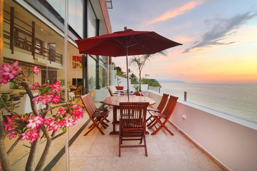 a table with an umbrella on a balcony with the ocean at Two-Story Beachfront Oasis in Puerto Vallarta