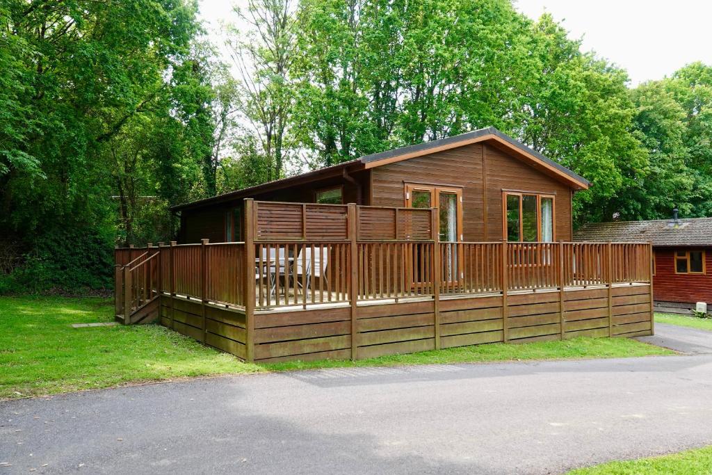 a wooden cabin with a fence in the grass at Charming Copse Corner Lodge - Spa Resort - Devon in Chudleigh