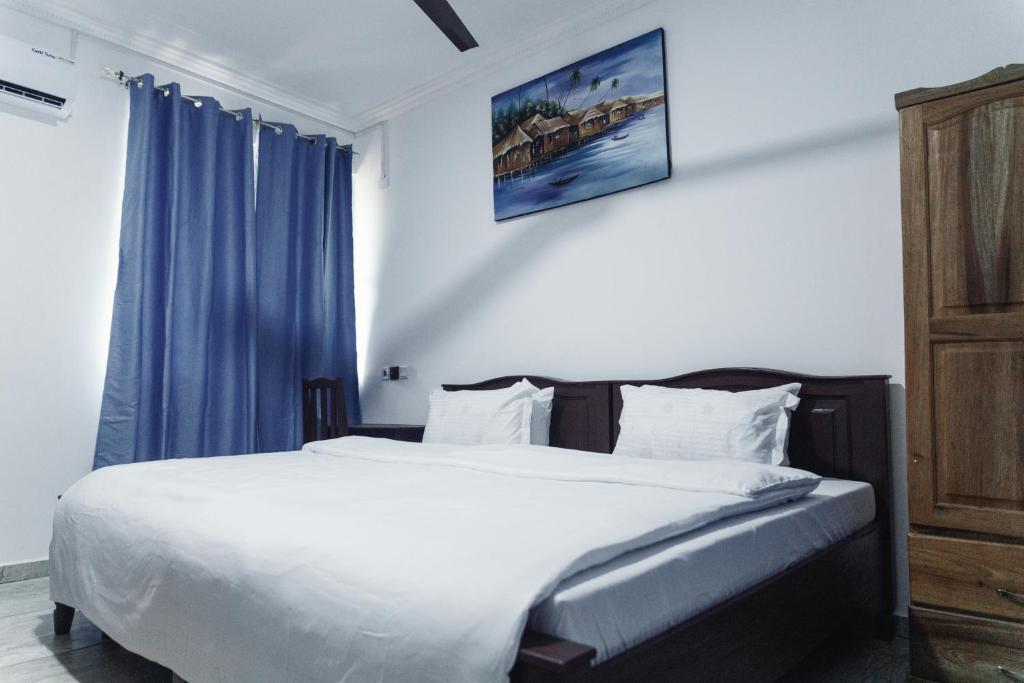 a bedroom with a large white bed with blue curtains at RAGANT Hotel in Cape Coast