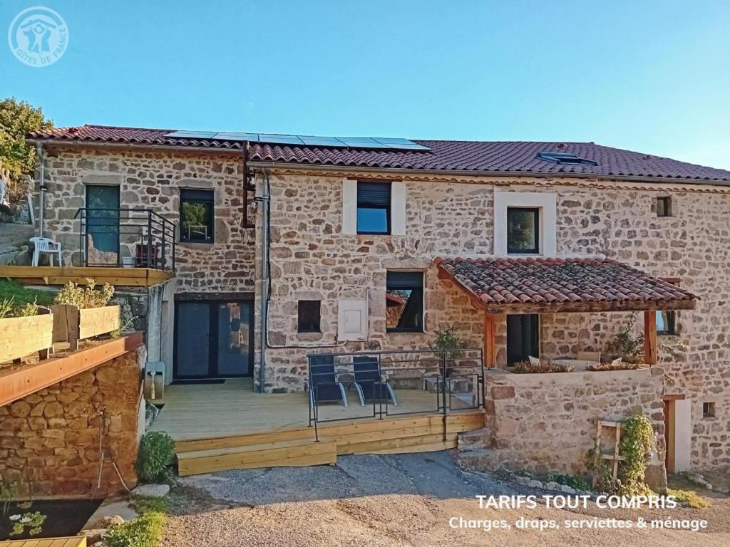 una casa in pietra con un ponte e sedie sopra di Séjour paisible en gîte de charme avec spa en campagne - FR-1-496-334 a Saint-Julien-Molin-Molette