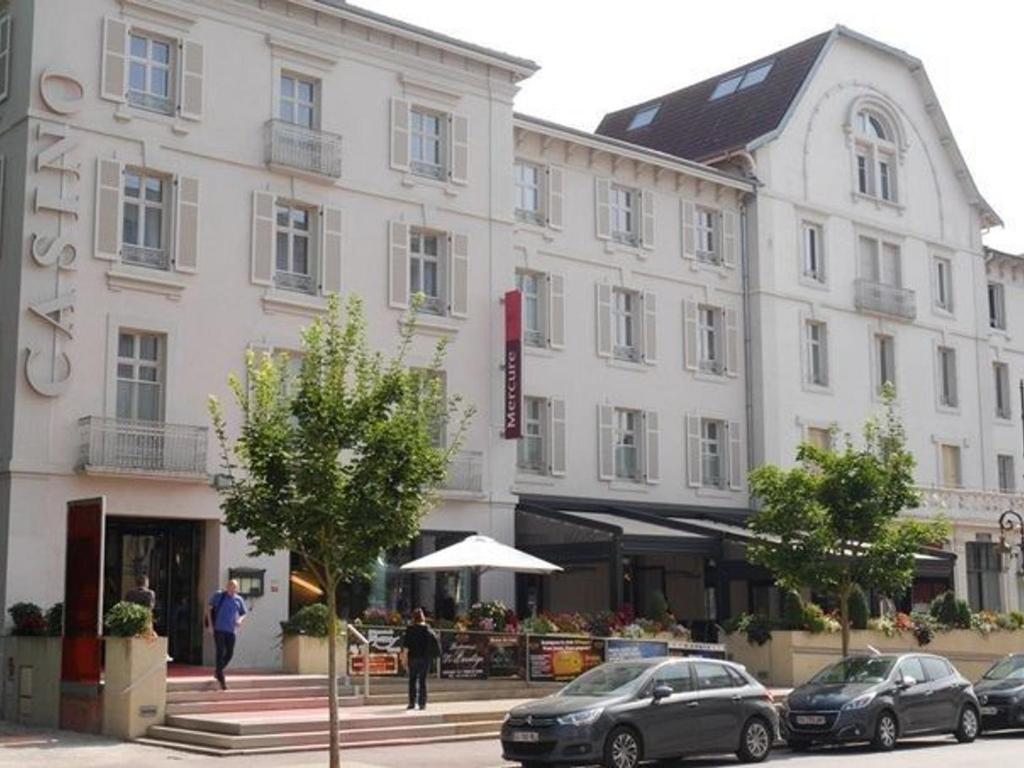 un grand bâtiment blanc avec des voitures garées devant dans l'établissement Appartement lumineux 4* pour 2 à Vittel, proche thermes, WiFi, parking gratuit - FR-1-589-745, à Vittel