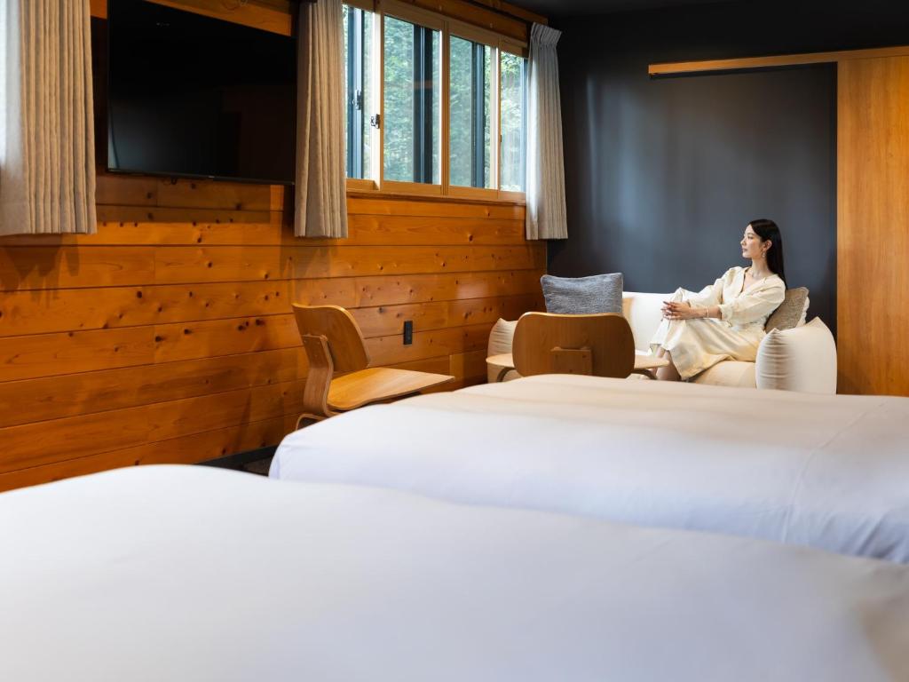 a woman sitting on a couch in a room with two beds at Kawaguchiko Country Cottage Ban in Fujikawaguchiko