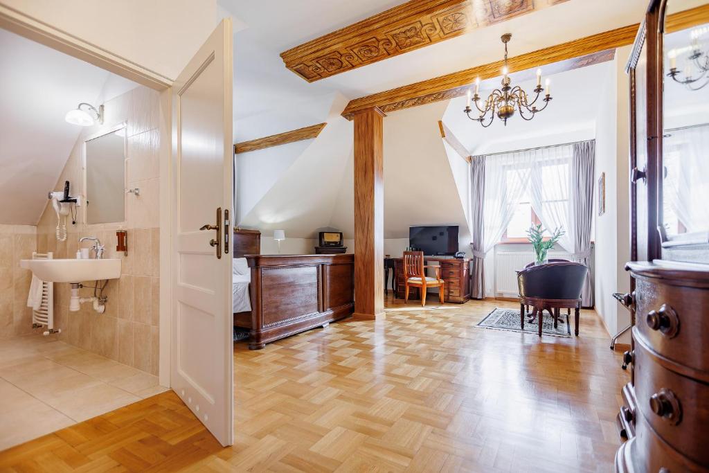 Spacious attic suite seen through open door with wooden beams, antique bed, desk, chandelier.