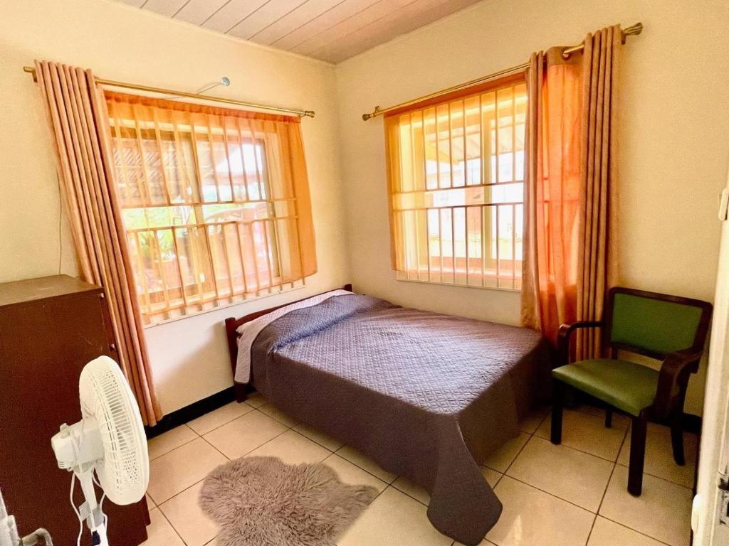 a bedroom with a bed and a chair and two windows at 3 Bed House - Sleeps 6 - Garden - Parking - Wifi in Paramaribo