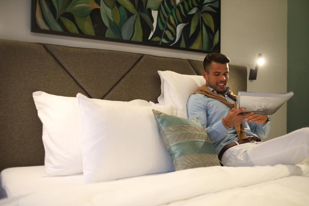 un uomo seduto su un letto che guarda un tablet di Hotel Botanica a Belgrado