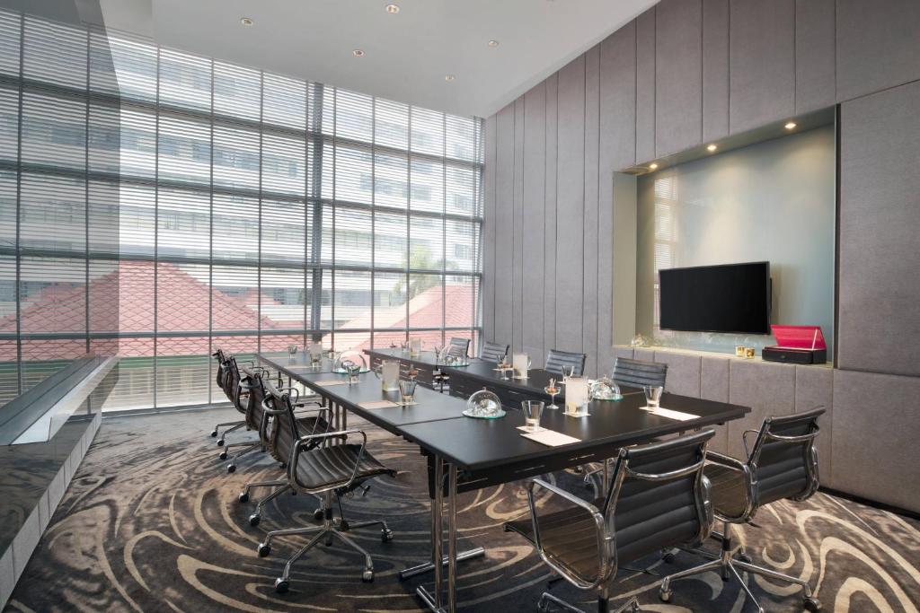 A bright boardroom with a long black conference table, rolling chairs and a wall-mounted screen.