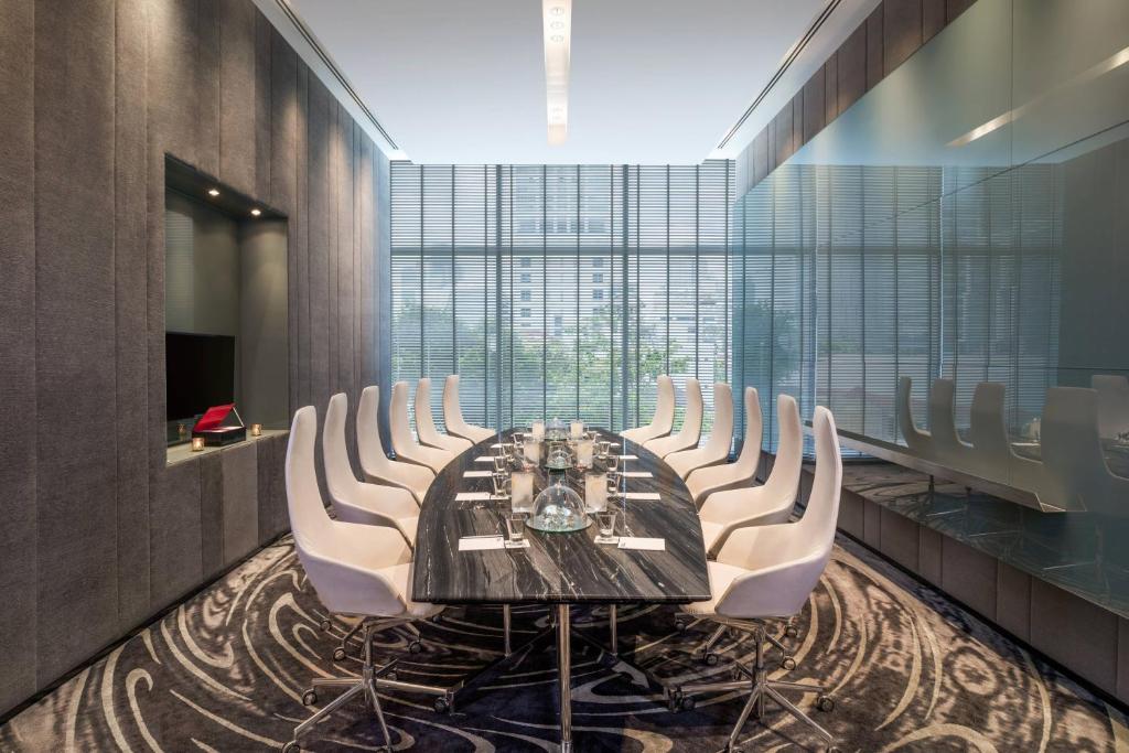 A compact boardroom with a long table, white chairs, presentation screen and reflective glass wall.