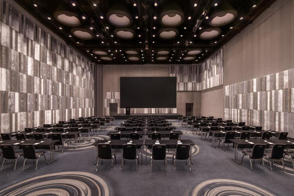 A large dark conference hall arranged classroom-style around a wide presentation screen.
