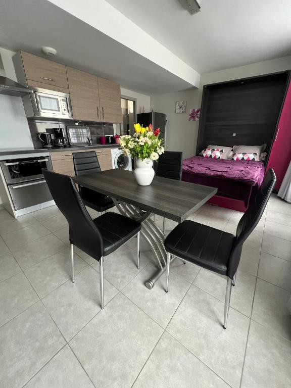 une table à manger avec des chaises noires et un vase avec des fleurs dans l'établissement Studio confortable à La Ferrière-aux-Étangs - 25 m² avec sauna, à La Ferrière-aux-Étangs