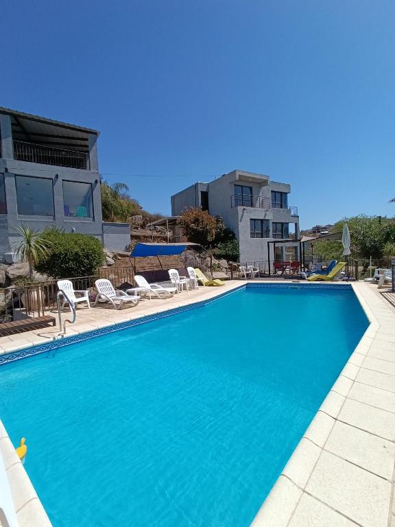 a large swimming pool with chairs and a house at Complejo Refugio Playa Perelli in Villa Carlos Paz