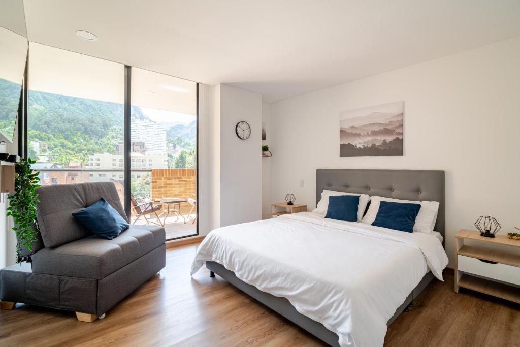 a white bedroom with a bed and a chair at Loft con vista única al Centro y Monserrate in Bogotá
