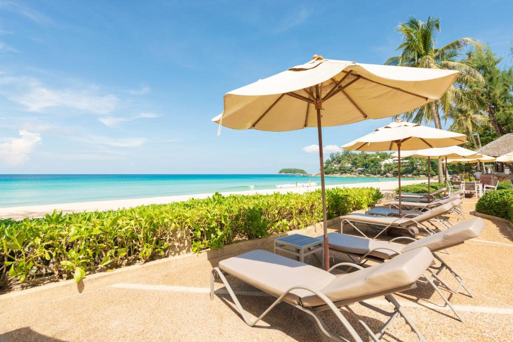 a row of beach chairs with an umbrella and the ocean at Katathani Phuket Beach Resort - SHA Extra Plus in Kata Beach