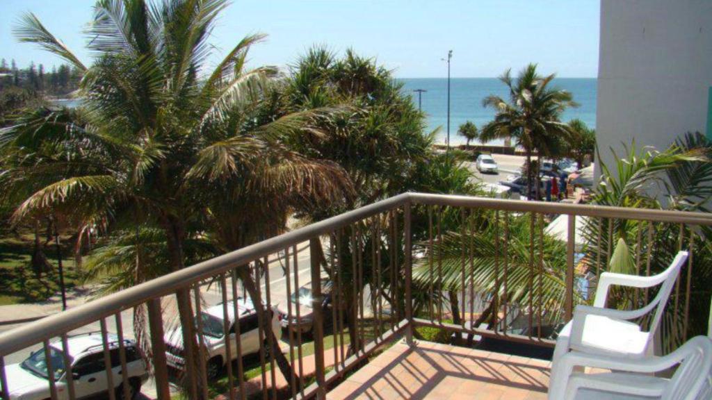 a balcony with a white chair and palm trees and the ocean at Seamist Lodge Unit 5 in Caloundra
