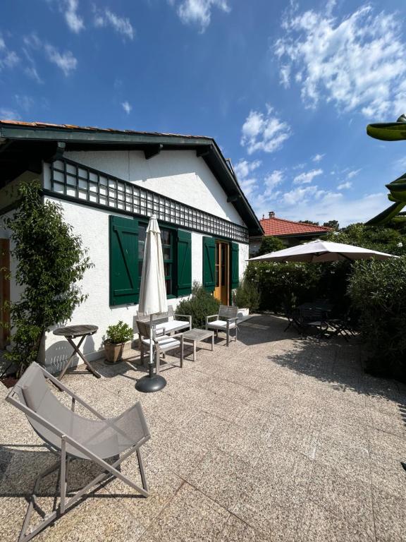 un patio avec des chaises et des parasols en face d'un bâtiment dans l'établissement Villa au Cap Ferret à 80mts de la plage et le marché, à Lège-Cap-Ferret