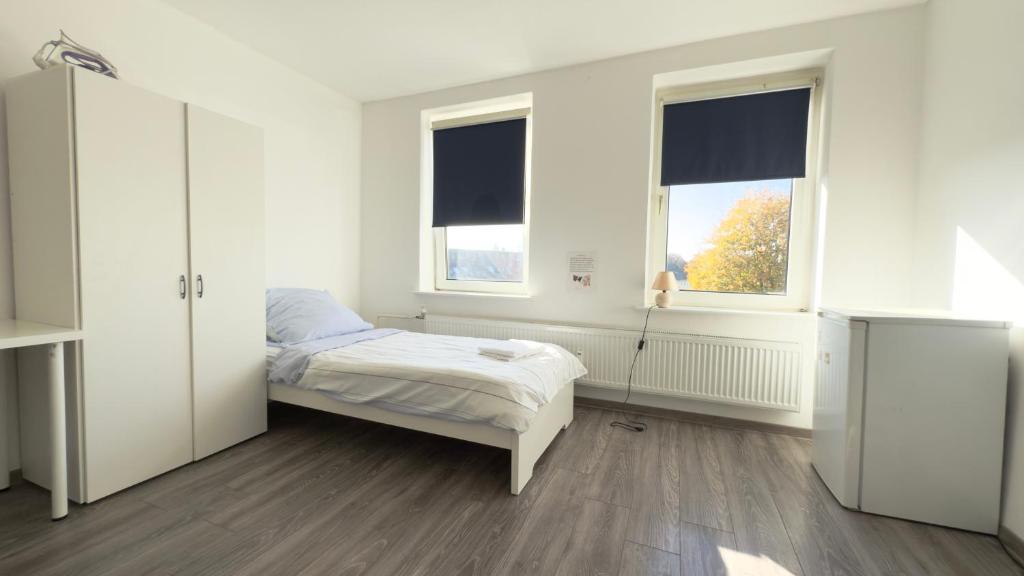 a white bedroom with a bed and two windows at Zentrale Monteurwohnungen in Neumünster ideal für Teams & Gruppen mit Küche & WLAN in Neumünster