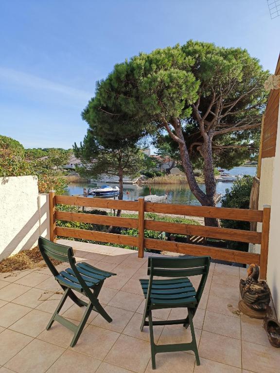 - deux chaises sur une terrasse avec un arbre et de l'eau dans l'établissement Maison Bord de lac 6 Personnes 2 Chambres, à Port-Leucate