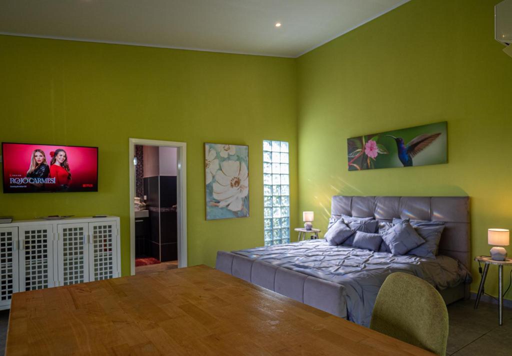 een slaapkamer met groene muren met een bed en een flatscreen-tv bij Finca Colibri in Boca Chica