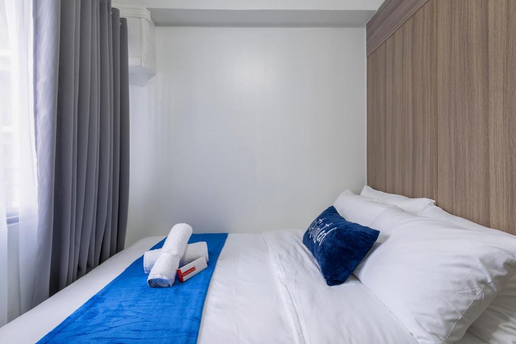 une chambre avec un lit aux draps blancs et aux oreillers bleus dans l'établissement Oasis Urban Stay 2, à Manille