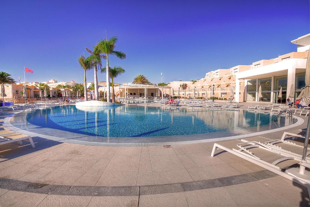 une grande piscine avec des chaises et des palmiers dans l'établissement SBH Monica Beach Resort, à Costa Calma