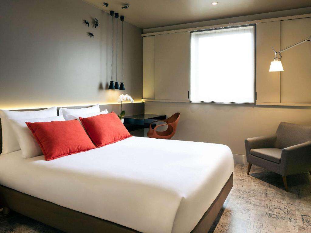 a bedroom with a bed with red pillows and a chair at Mercure Porto Centro Santa Catarina in Porto