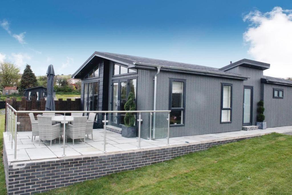 una casa con terraza con mesa y sillas en Nyth Glan y Môr, Modern Luxury Lodge with Hot Tub, en Pembrokeshire