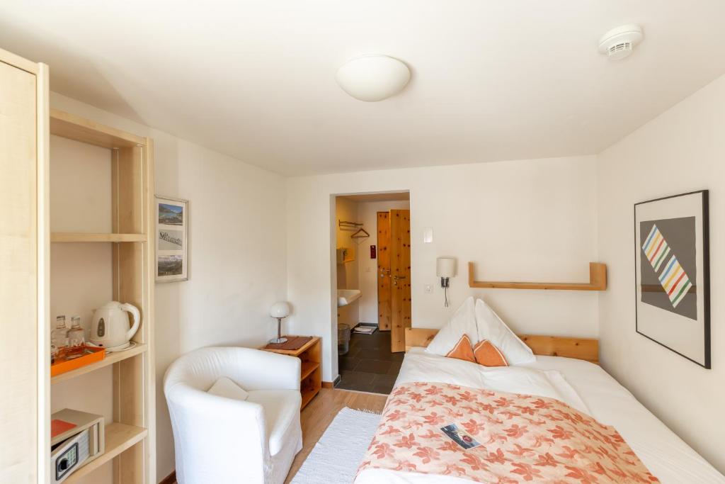 a bedroom with a bed and a white chair at Palazzo Mysanus Samedan in Samedan