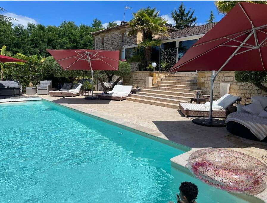 una piscina con ombrelloni rossi e una casa di Gîte 1 à 6 personnes Rez de jardin de la villa piscine et sauna à partager Jacuzzi en option a Sarlat-la-Canéda