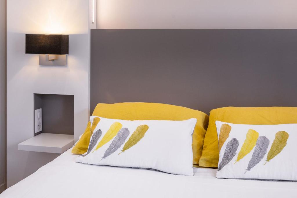 a bed with yellow and white pillows on it at Le Cornouaille Hotel & Spa in Bénodet