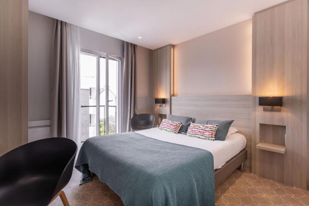a bedroom with a bed with two chairs and a window at Le Cornouaille Hotel & Spa in Bénodet