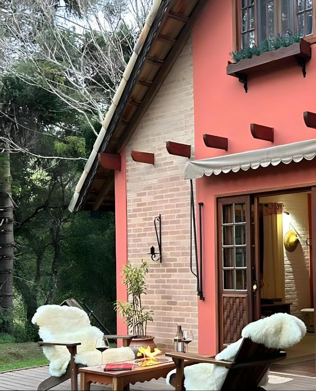 a red house with two chairs and a table at CHALÉ AZALÉA Lindo chalé NO CAMPO com roupas de cama e banho impecáveis, Wi-Fi StarLink de alta velocidade, cozinha equipada, estacionamento privativo, decks, jardins, lareiras, conforto, privacidade e belíssimas paisagens in Cunha