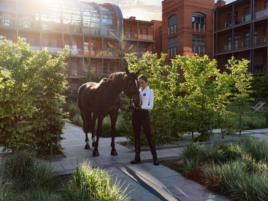 a woman standing next to a brown horse on a sidewalk at City Park Hotel & Residence in Poznań