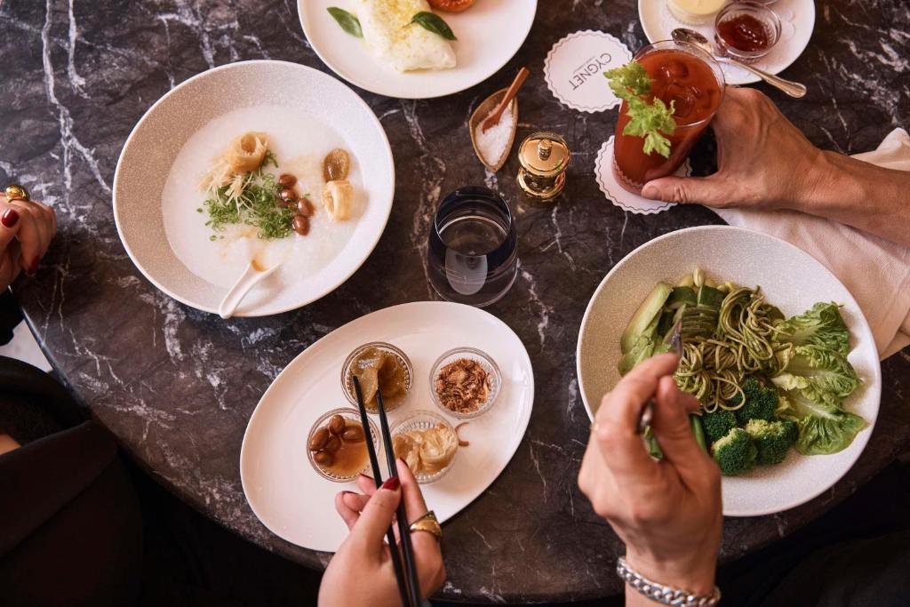 a table with plates of food and people holding spoons at QT Singapore in Singapore