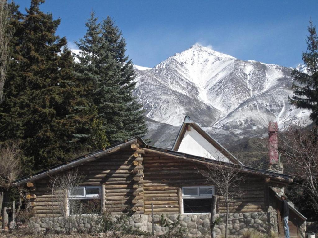 a log cabin with a snow covered mountain in the background at Anthar Andes in Potrerillos