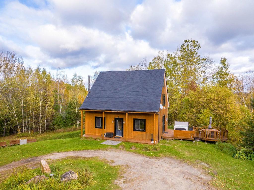 a small house with a black roof on a field at Au Chic Chalet des Chutes Chic Cottage in Sainte-Melanie