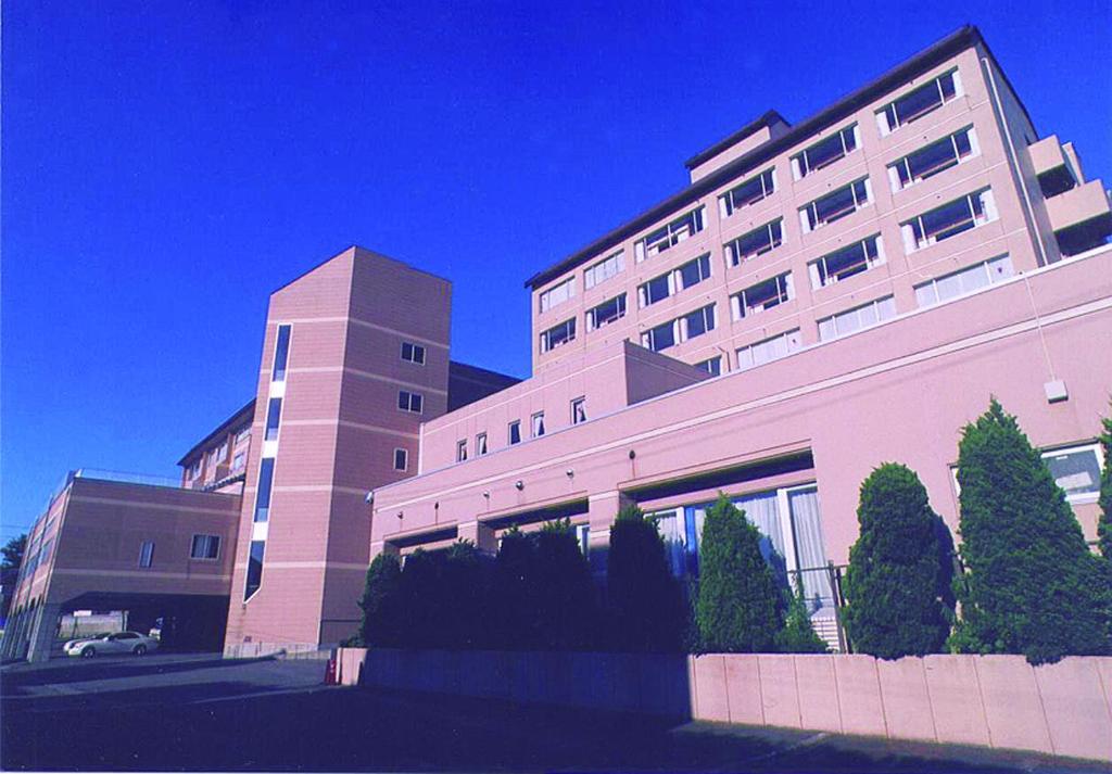 un grande edificio con alberi di fronte di Hotel Tetora Resort Tsuruoka a Tsuruoka