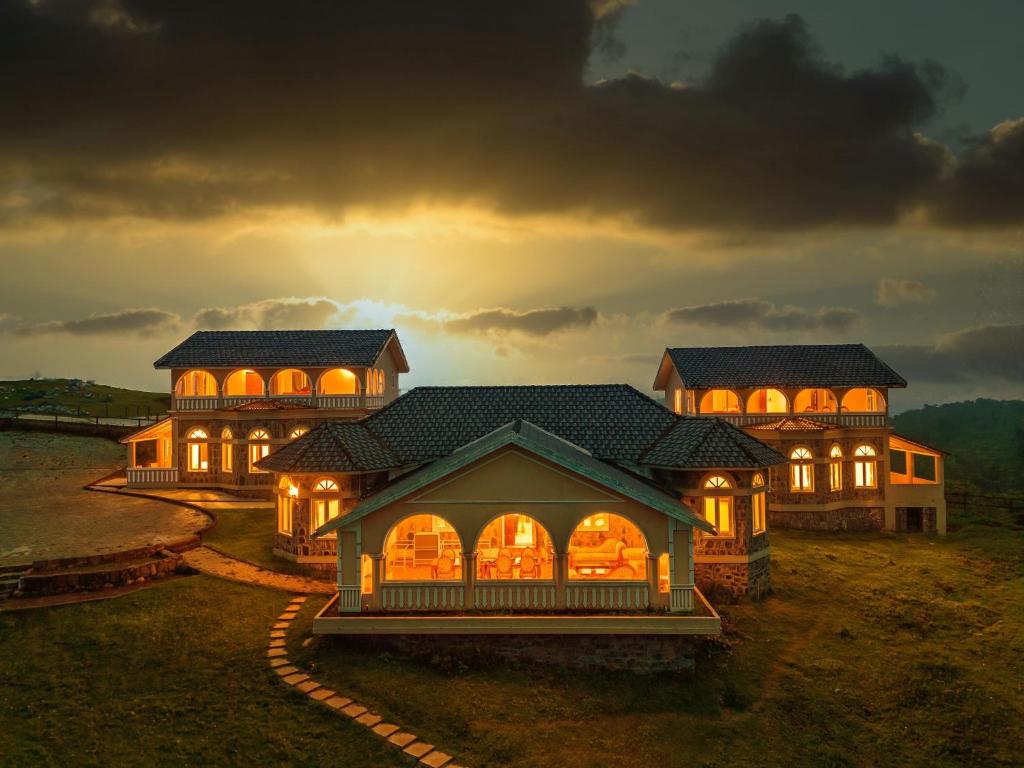 una casa grande con sus luces encendidas por la noche en Emerald Stays Ooty By VOYE HOMES - Italian Luxury near Ooty Emerald Lake, en Ooty