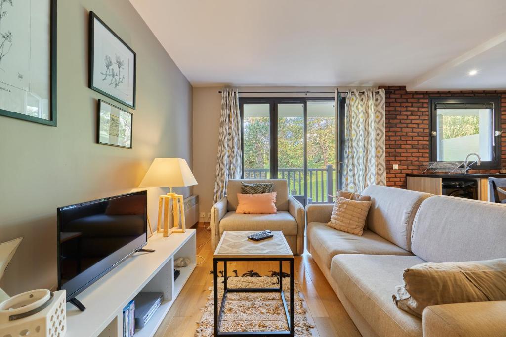 un salon avec un canapé et une télévision dans l'établissement Une Parenthèse à la Mer - Appt vue mer, à Blonville-sur-Mer