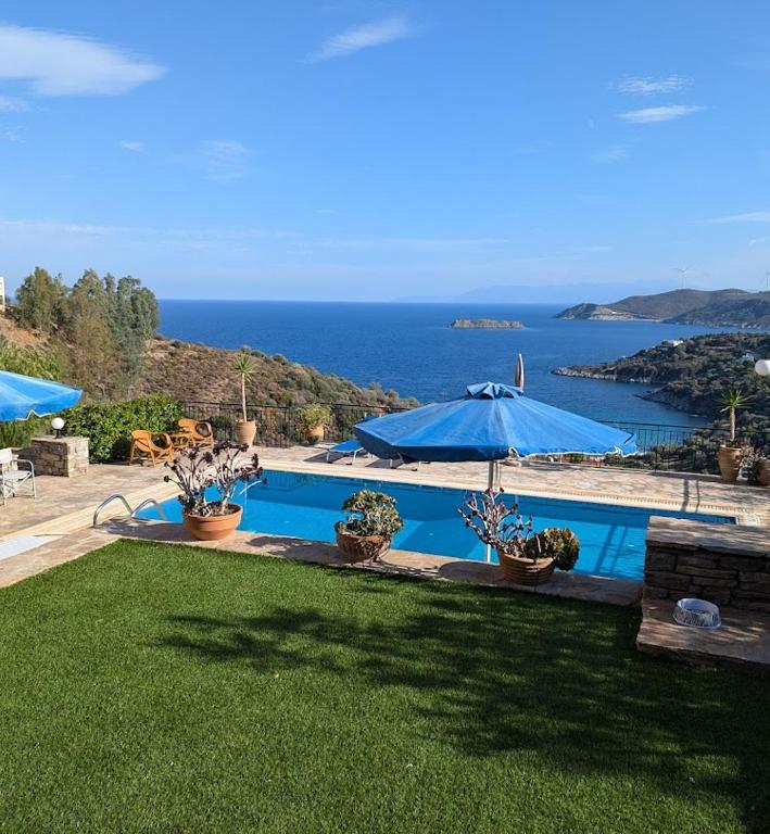 a swimming pool with a blue umbrella and the ocean at Villa Lumière- Avantes in Agioi Apostoli
