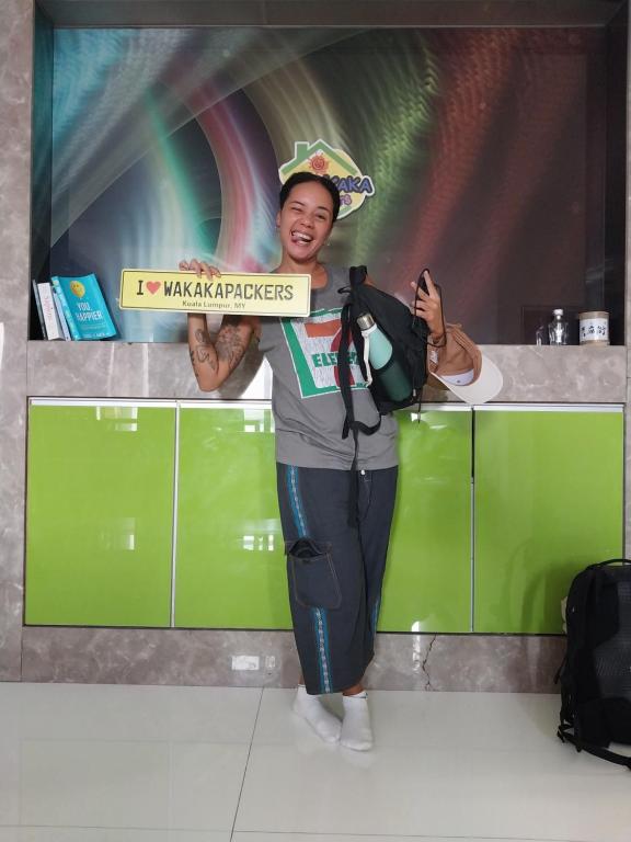 a man is holding up a sign in front of a counter at WakakaPackers in Kuala Lumpur