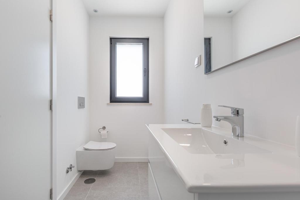 a white bathroom with a toilet and a sink at Villa Locki in Lourinhã