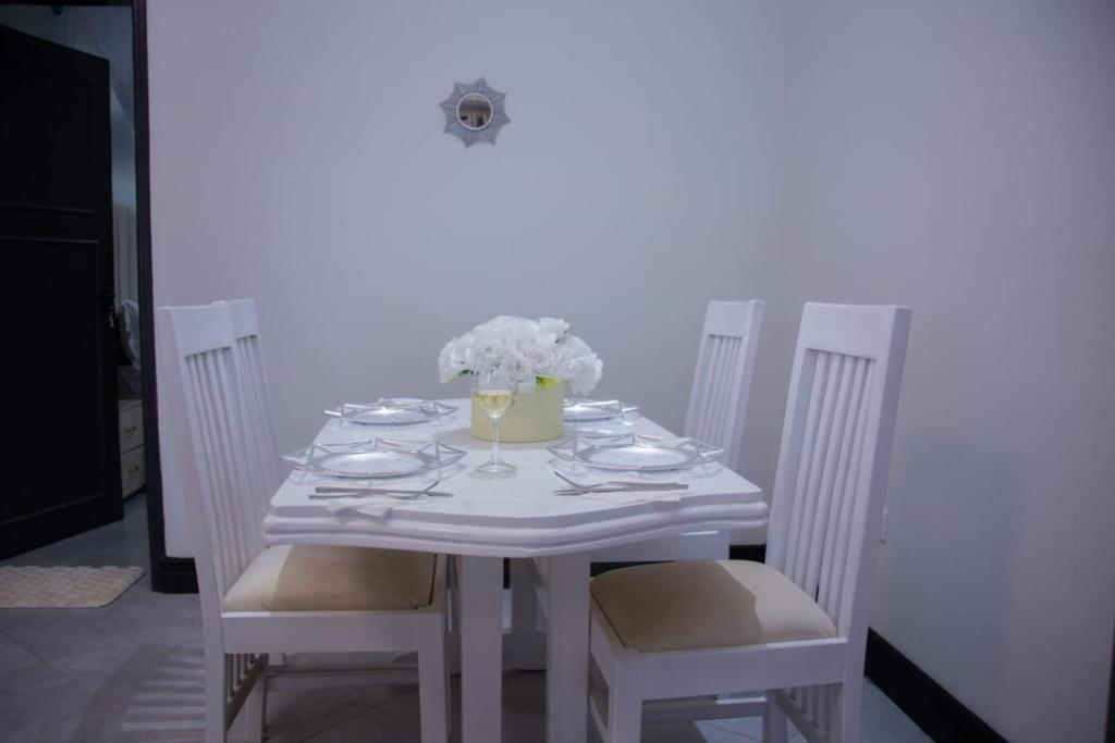 een witte tafel met stoelen en een vaas met bloemen bij Safari Apartments in Munyonyo