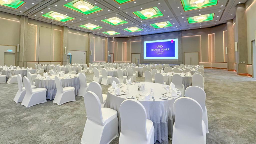 a banquet hall with white tables and chairs and a screen at Crowne Plaza Bahrain by IHG in Manama