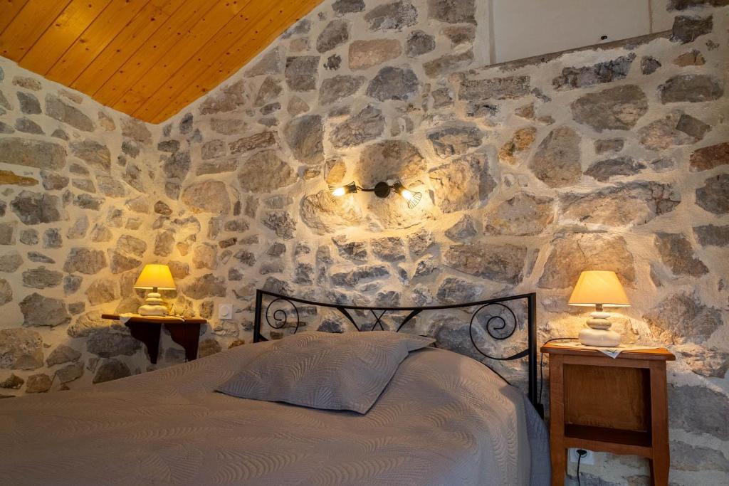 - une chambre dotée d'un mur en pierre avec un lit et deux lampes dans l'établissement La maisonnette a la caze, à Saint-Pierre-des-Tripiers