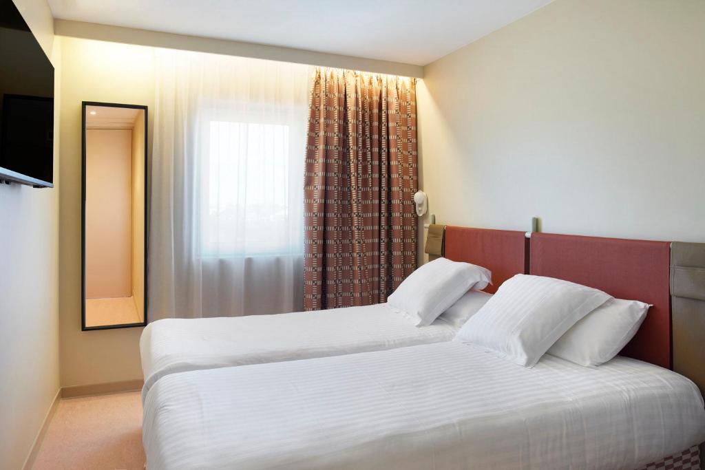a bedroom with a bed with white sheets and a window at Hotel des Victoires - Restaurant in Cannes