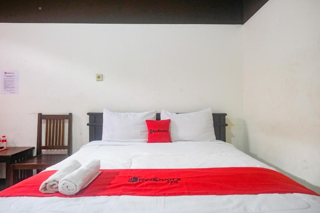 a white bed with red and white pillows on it at RedDoorz at Mayang Garini 2 Borobudur in Magelang