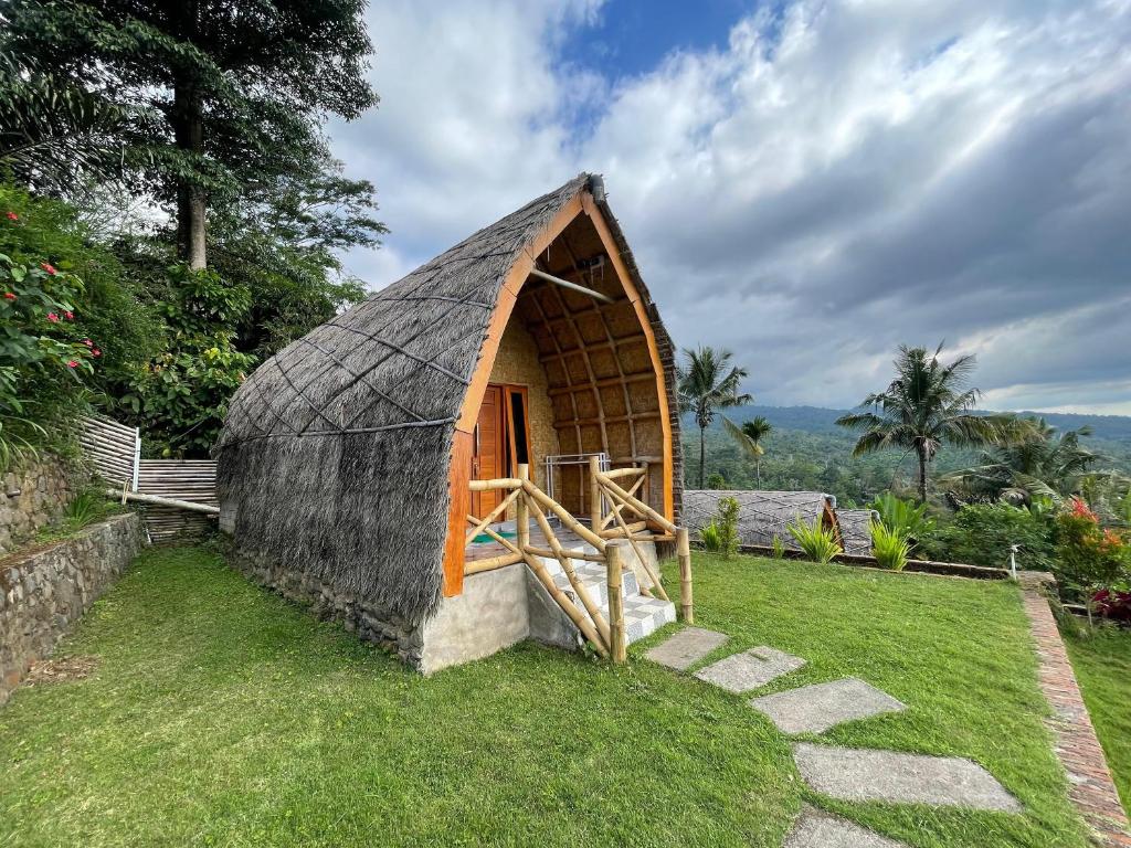 a small house with a thatched roof on the grass at Villa Bambu Rinjani & Restaurant in Senaru
