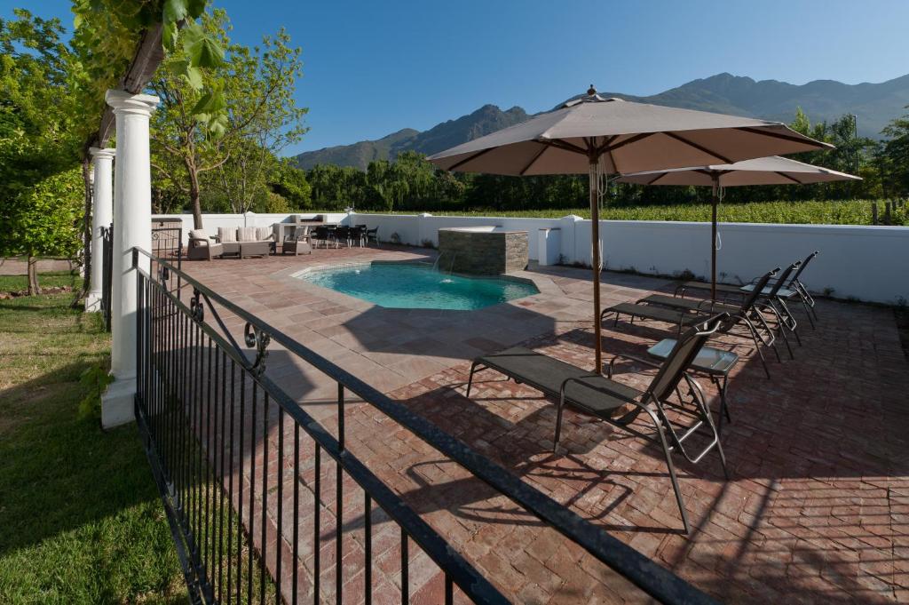 un patio con sillas, una sombrilla y una piscina en La Galiniere Guest Cottages, en Franschhoek