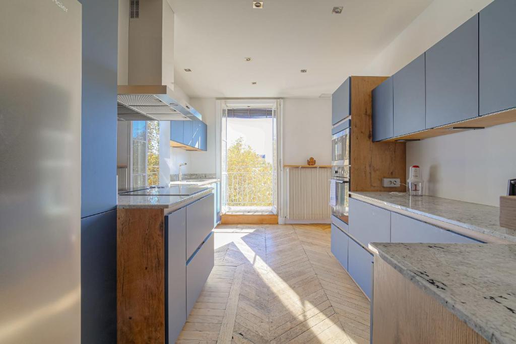 une grande cuisine avec des placards bleus et une grande fenêtre dans l'établissement Spacieux et Charmant 150m2 Place Maréchal Lyautey, à Lyon