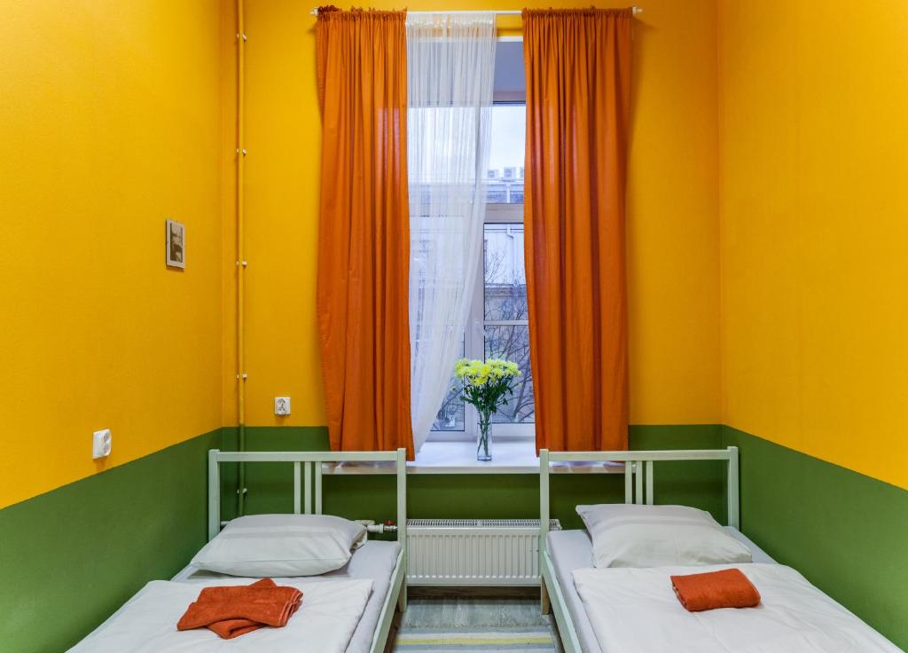 2 Betten in einem Zimmer mit gelben Wänden und einem Fenster in der Unterkunft Na Italyanskoy Mini-Hotel in Sankt Petersburg