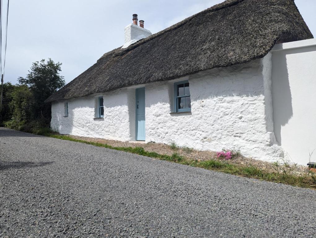 a white cottage with a thatched roof on a road at Goggin Cottage in New Kildimo